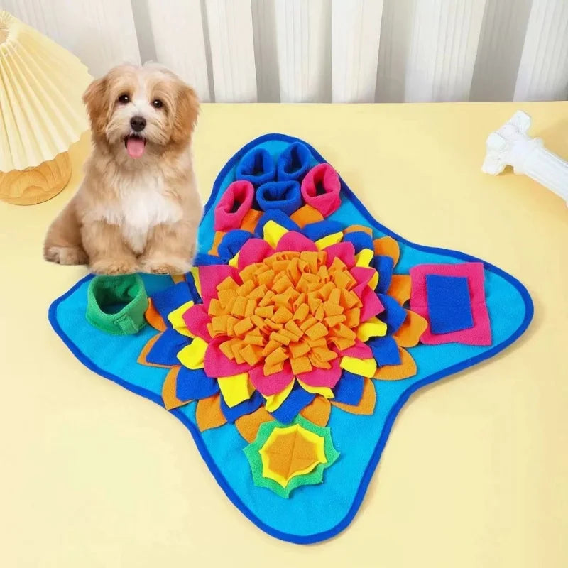 A fluffy light brown dog is sitting next to a colorful, interactive sniffing mat for pets on a yellow surface.