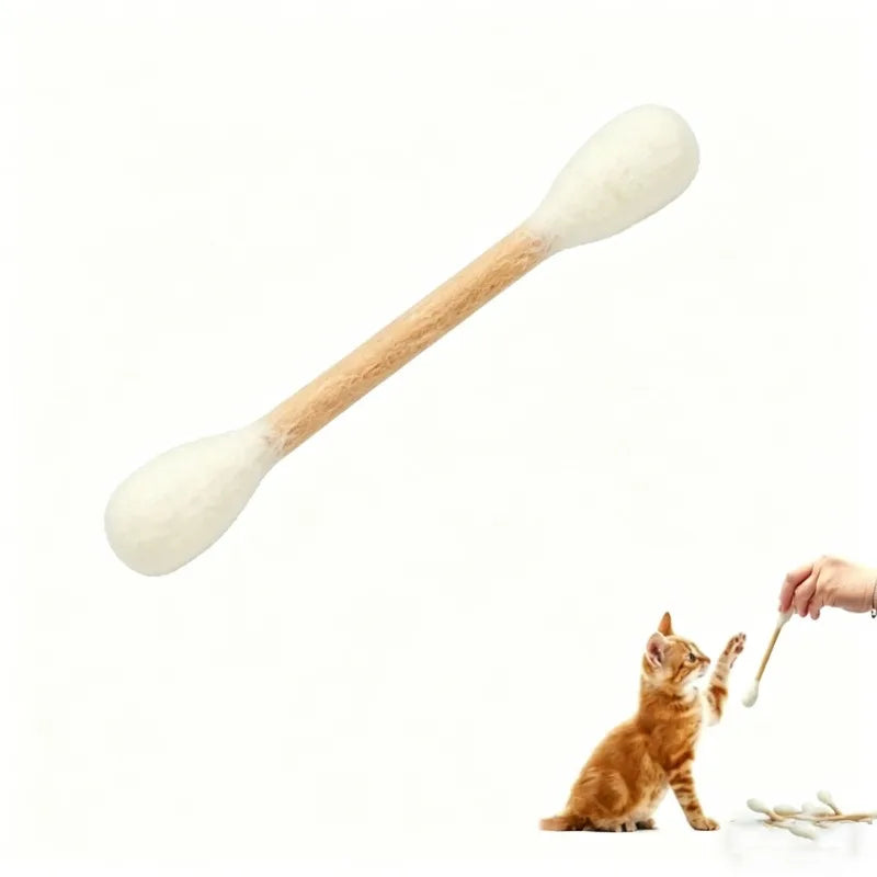 Una espátula de madera con forma de gato junto a un gatito naranja.