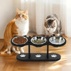 A black elevated cat food bowl stand holding three stainless steel bowls with dry food.
