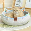 A fluffy orange tabby cat is relaxing in a woven cat scratcher and comfort bed filled with colorful play balls.