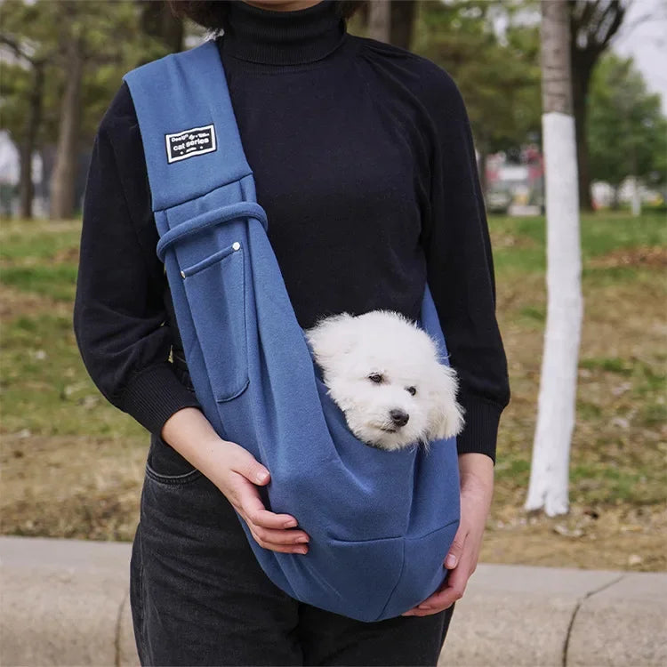 Eine Person hält einen marineblauen, leichten Hundeträger mit einem weißen flauschigen Hund im Freien.
