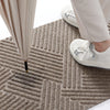 A close-up view of a beige textured geometric doormat with vertical lines, showing a person's legs and white sneakers on the 