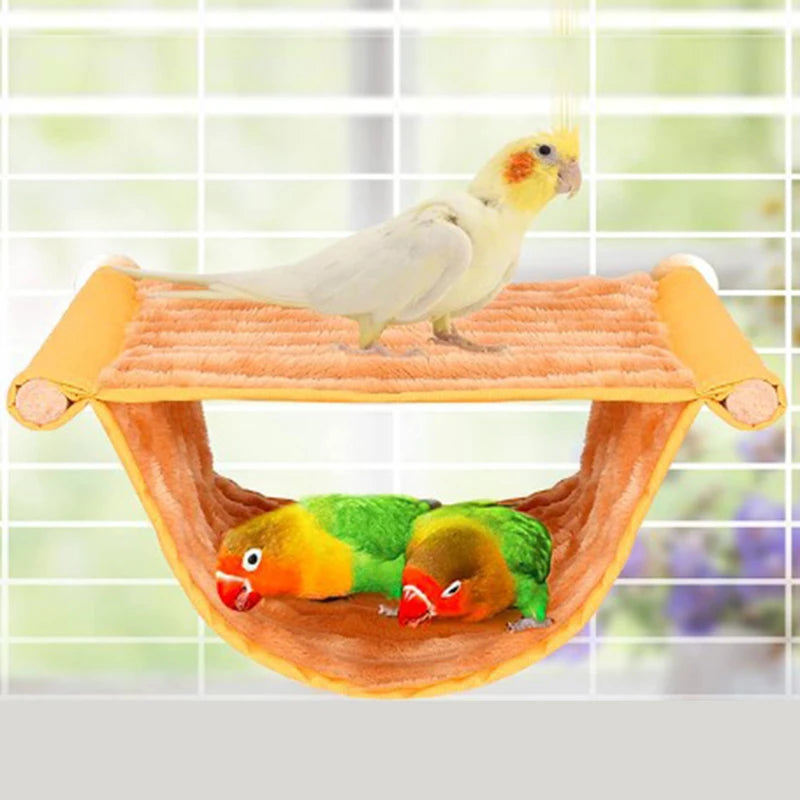 A yellow and green parrot is perched on a cozy orange fleece bird hammock.