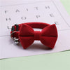 A red plush velvet pet collar featuring a bow and a silver bell, resting on a white paper with inspirational words.