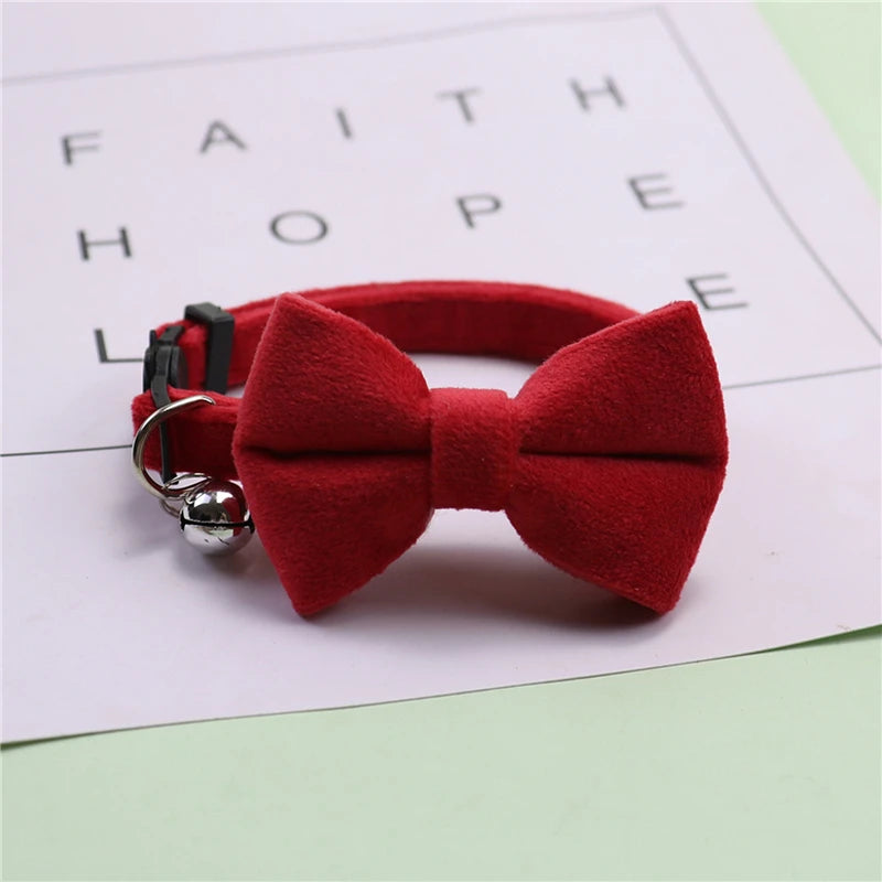 A red plush velvet pet collar featuring a bow and a silver bell, resting on a white paper with inspirational words.