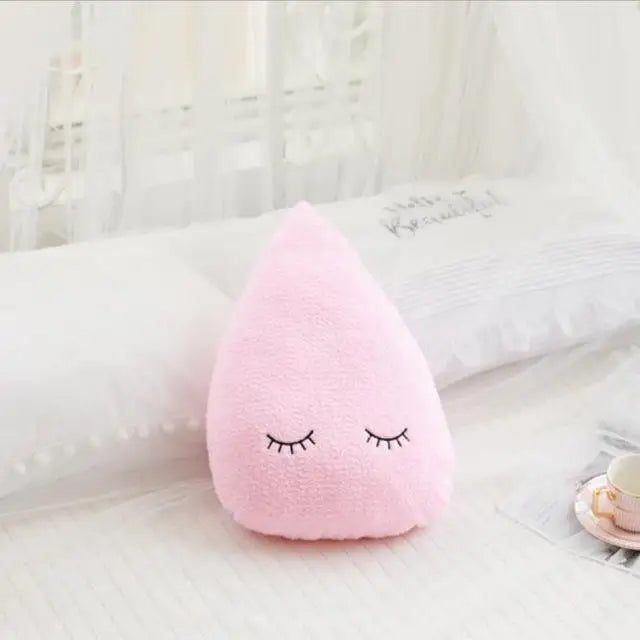 A pink cloud shaped plush pillow with closed eyes resting on a white bed.