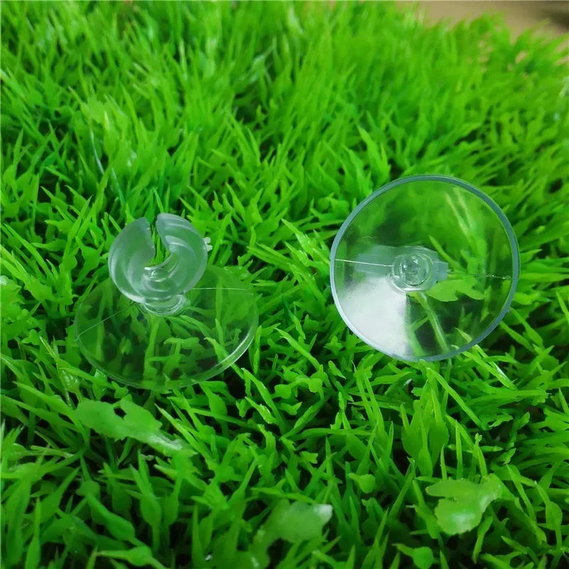 A clear suction cup for aquarium air line, shown resting on bright green artificial grass.