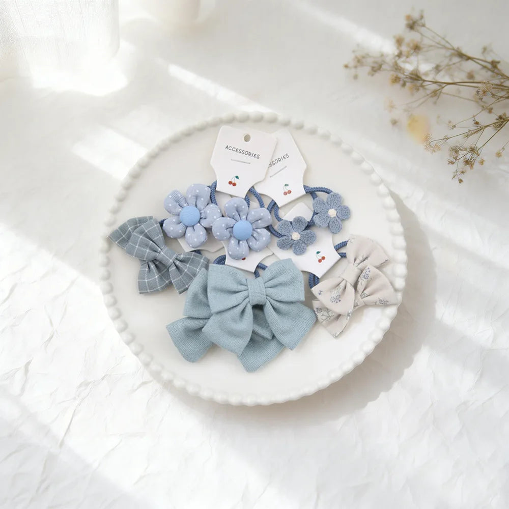 Collection de nœuds pour cheveux et accessoires en tissu bleu clair et gris présentés sur une assiette blanche.