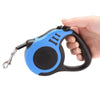 A hand is holding a blue and black automatic retractable dog leash.