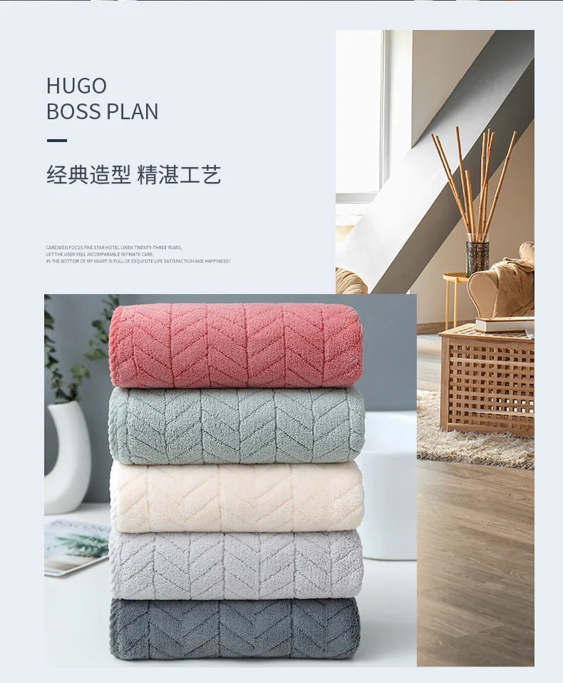 A stack of five plush microfiber bath towels in shades of pink, green, beige, gray, and blue.