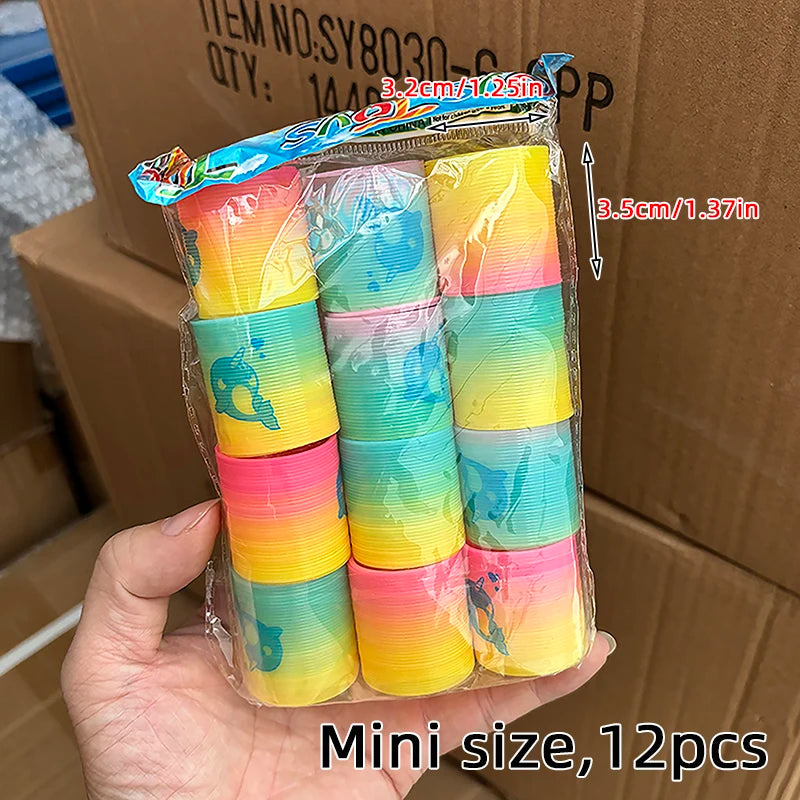 A hand holds a clear plastic package containing 12 colorful rainbow spring coil toys.