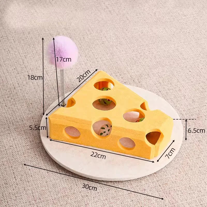 A yellow felt cat maze play box with holes and a purple pom-pom teaser toy is shown on a light surface.