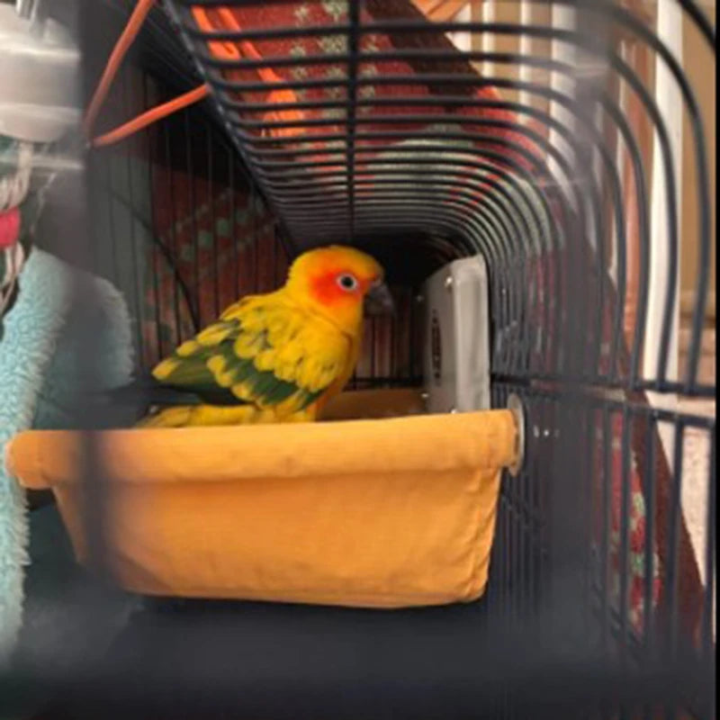 A yellow and green parrot is resting in an orange dish inside a black bird cage.