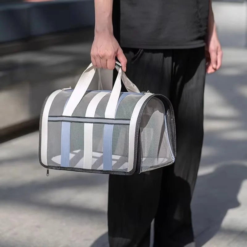 A person holds a gray and white striped lightweight foldable mesh travel carrier bag for small pets.