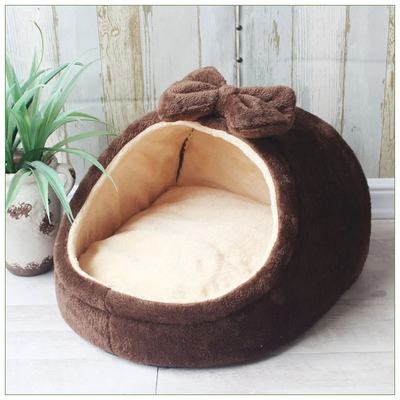 A dark brown, plush pet bed with a bow, lined with light tan fabric, resting on a light wooden floor.