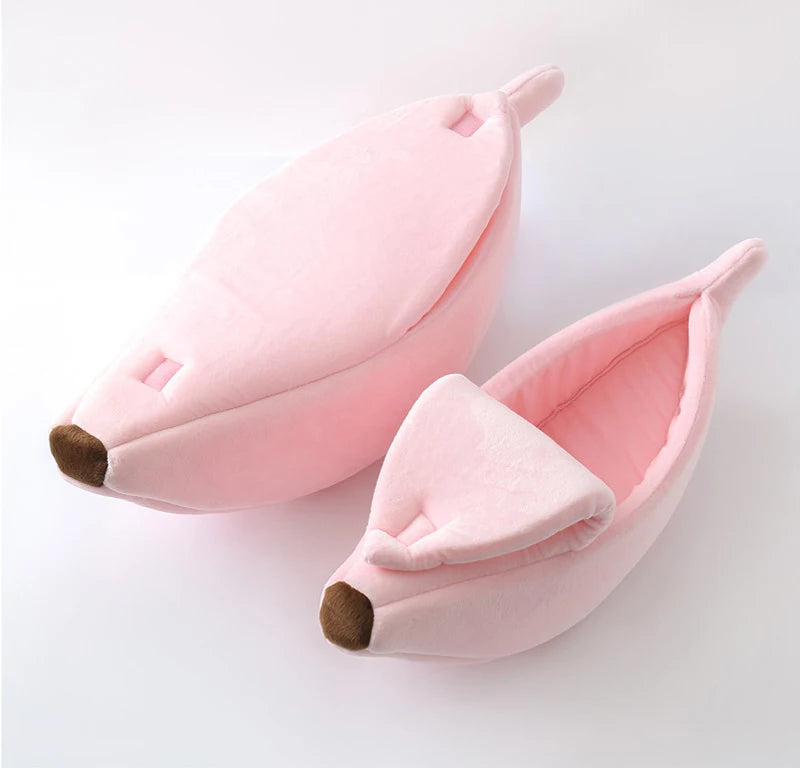 Un lit pour animal de compagnie rose en forme de banane avec des oreilles douces et un nez brun sur fond blanc.