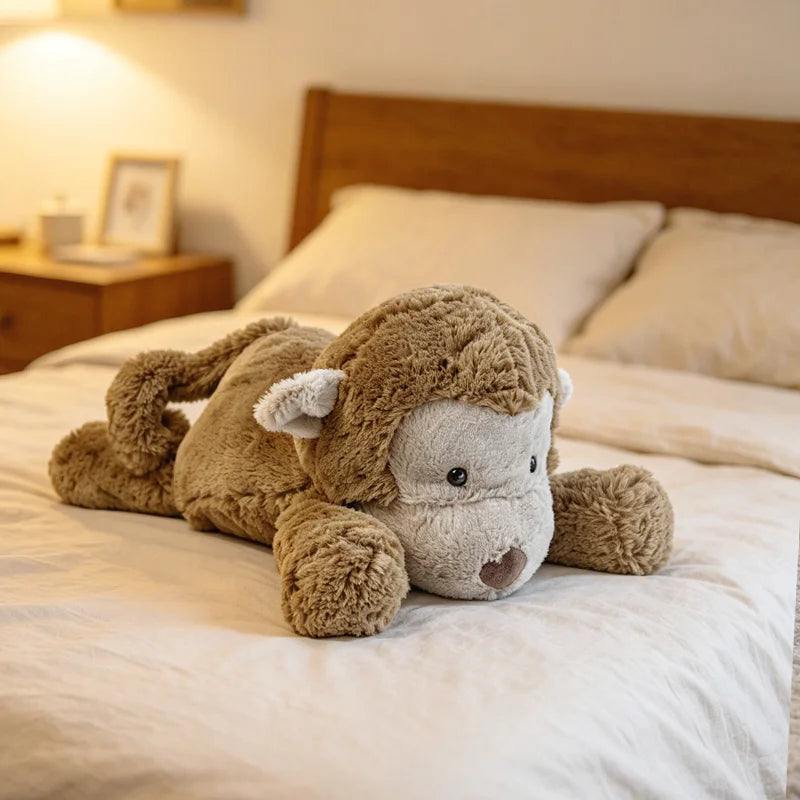 A soft, brown elephant monkey plush toy lying on a white bed with light bedding.