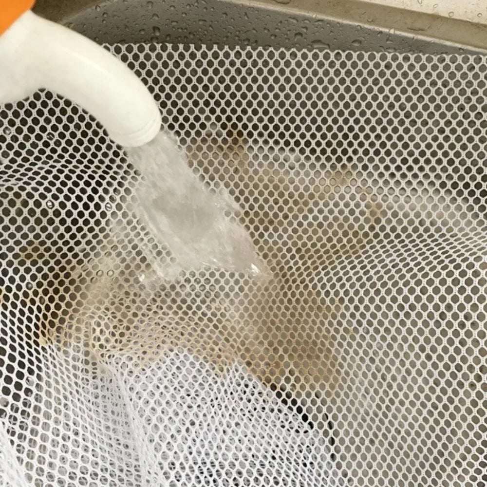 A white liquid is being poured into a gray mesh laundry bag inside a washing machine drum.