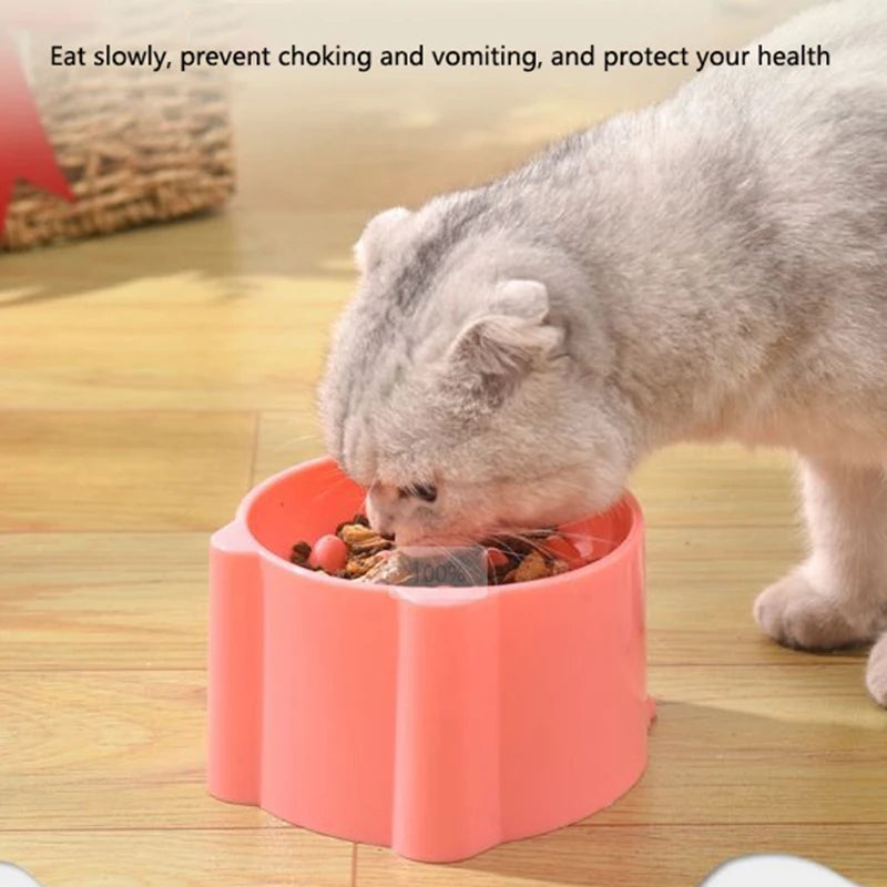 A cat is eating food from a pink anti-choking slow feeder bowl on a wooden surface.