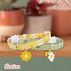 A yellow floral breakaway cat collar with a bell and a green floral breakaway cat collar are displayed on a wooden surface.
