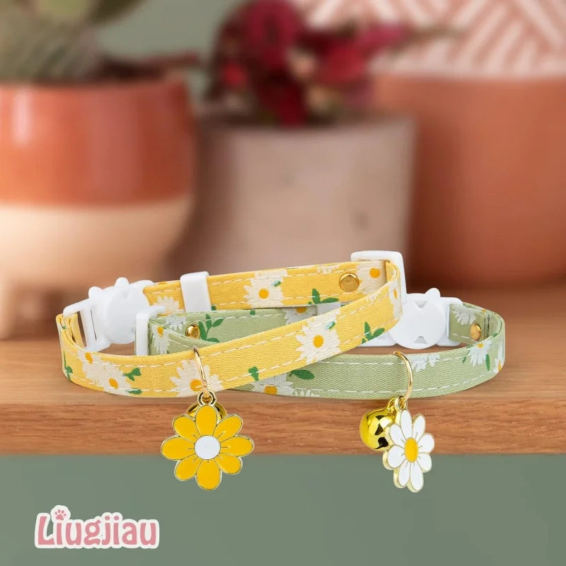 A yellow floral breakaway cat collar with a bell and a green floral breakaway cat collar are displayed on a wooden surface.