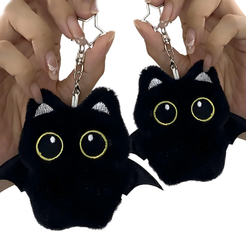 A black cat plush pendant with gold accents is being held by a person, showing its detail and size.
