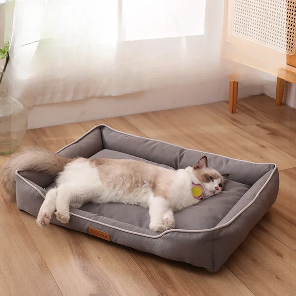 A fluffy white and gray cat is relaxing on a gray faux fleece pet sofa bed indoors.