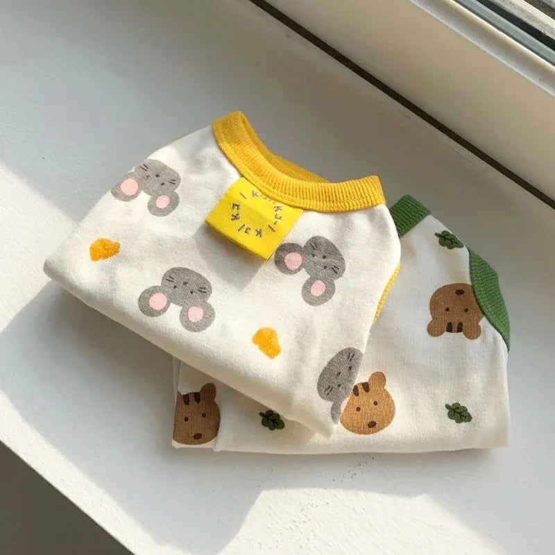 A white lightweight summer dog vest with a cute bear print and yellow trim is displayed on a window ledge.