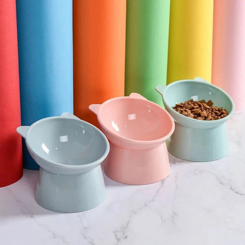 A set of five colorful pet feeding bowls in shades of blue, orange, green, yellow, and pink are displayed on a white marble s