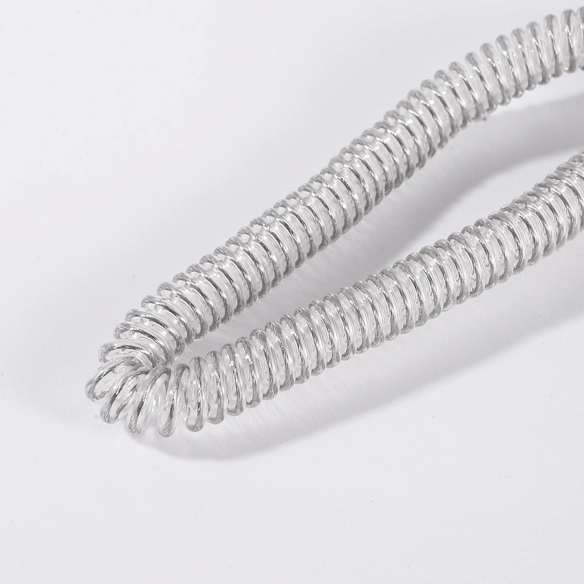 A close-up of a silver stretch bird flying leash coiled and laid out on a white surface.