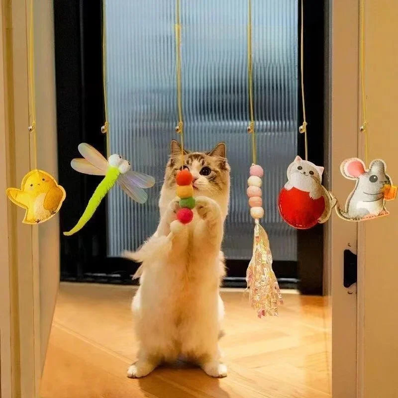 A fluffy cat hangs from a rope toy featuring colorful, dangling toys like a yellow ball and a green feather.