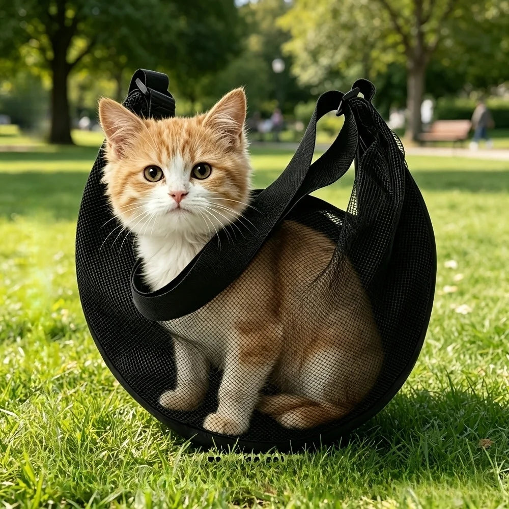 A fluffy orange and white kitten is sitting inside a black breathable pet carrier sling on green grass.