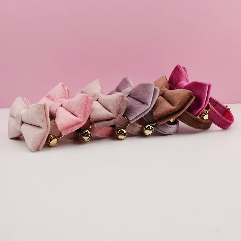 A collection of velvet cat collars in various shades of pink, mauve, and brown with gold-toned bell accents.