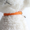 An adjustable cat collar made of soft orange PU leather with a metal bell attached, shown against a white fluffy background.