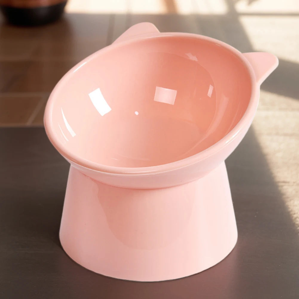 A pink ergonomic tilted cat food bowl with a non-slip base sitting on a dark surface.