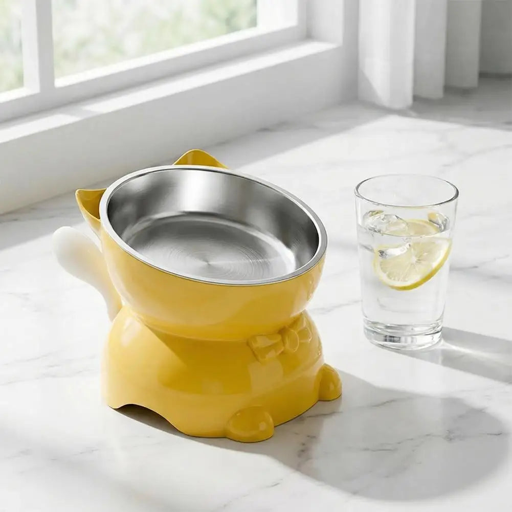 A yellow elevated cat bowl with a stainless steel insert sits on a white marble surface next to a glass of water.