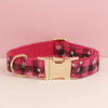 A pink plaid dog collar with a gold buckle and white snowflake pattern on the fabric.