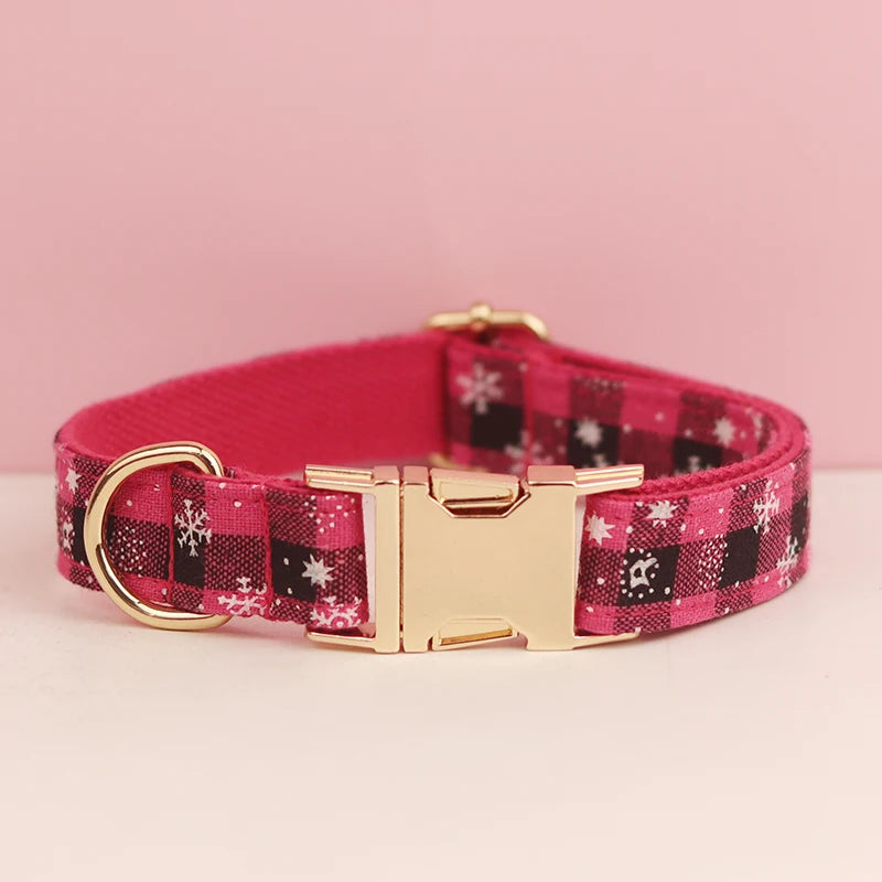 A pink plaid dog collar with a gold buckle and white snowflake pattern on the fabric.