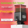 A black automatic fish feeder with a clear tank and LCD screen is shown on a white surface.