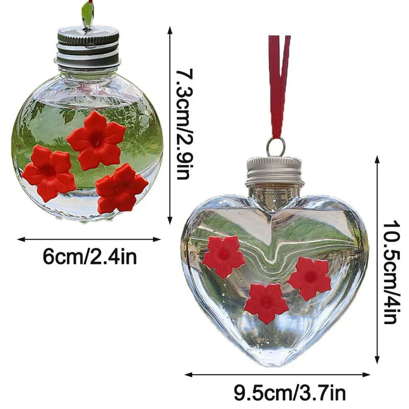 A clear glass hanging bird water feeder shaped like a heart with red flowers.