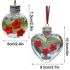 A clear glass hanging bird water feeder shaped like a heart with red flowers.