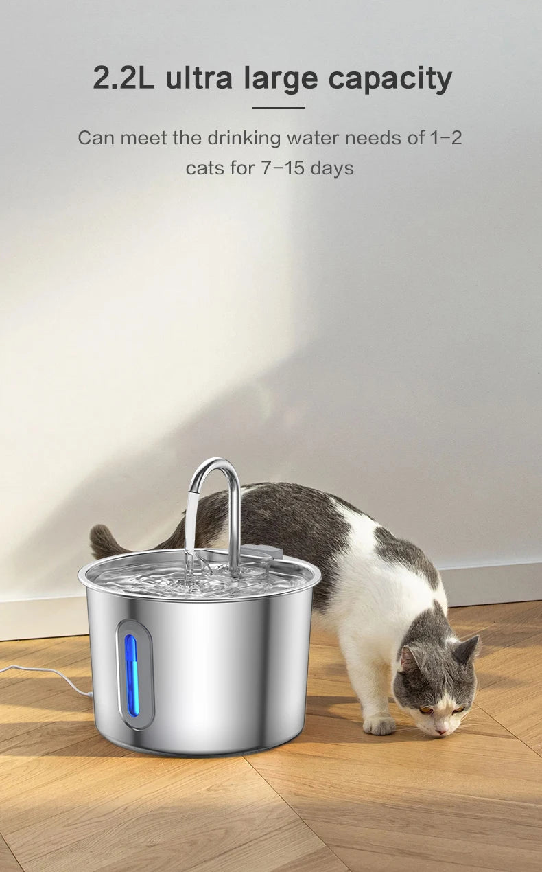 A silver stainless steel pet water fountain is shown with a cat drinking water from it on a wooden floor.