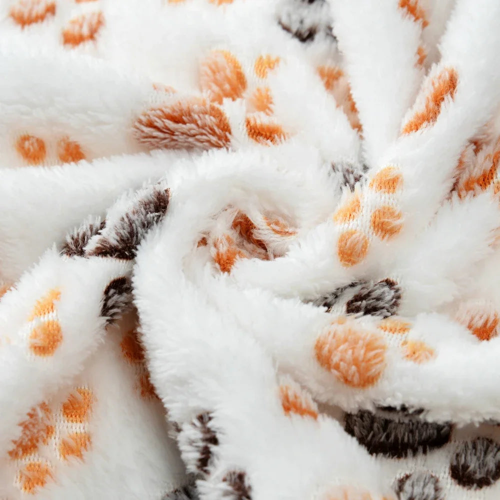 White fleece pet blanket with an orange and gray paw print pattern, rolled up.
