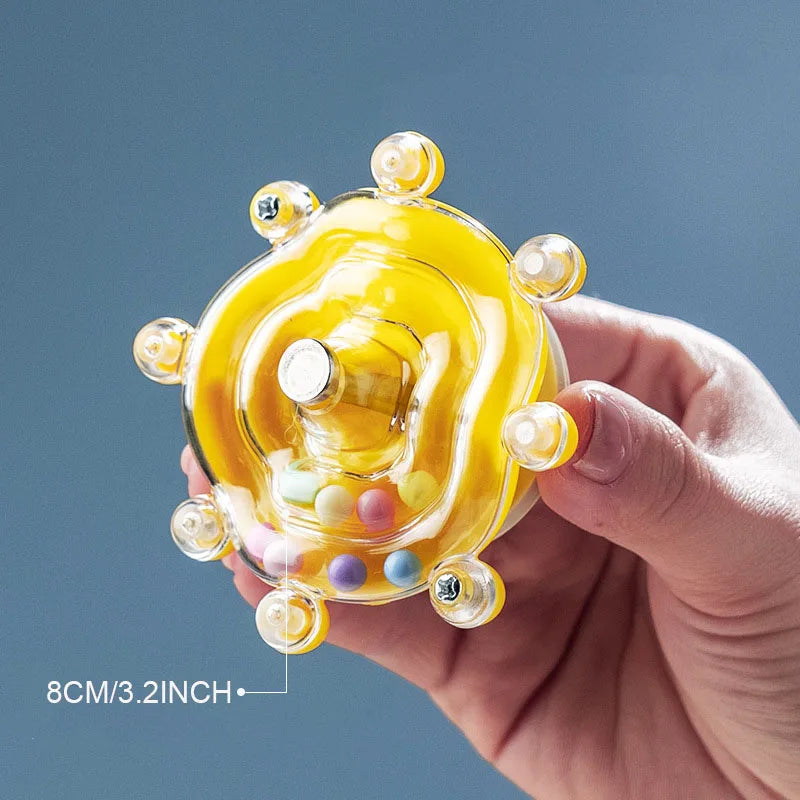 Eine Hand hält einen gelben, runden, interaktiven Leckerli-Dispenser mit kleinen bunten Bonbons.