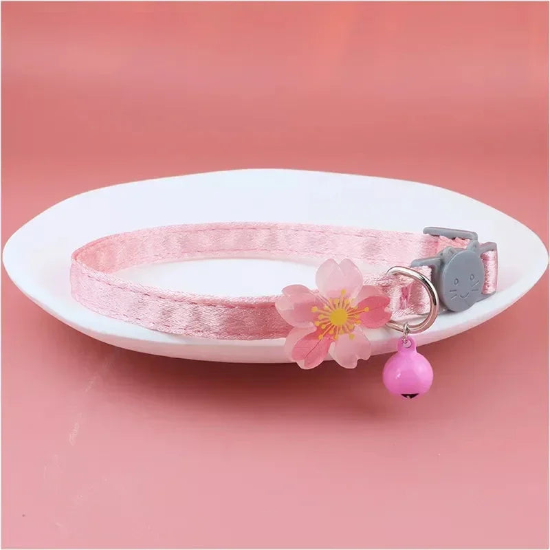 Pink lace bow cat collar with a bell and a pink bead charm displayed on a white plate.