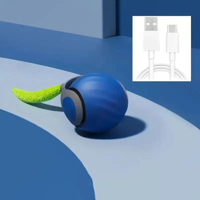 Blaues, kugelförmiges Katzenspielzeug mit grünem, flauschigem Anhängsel auf blauer Oberfläche neben einem weißen Elektrikstec