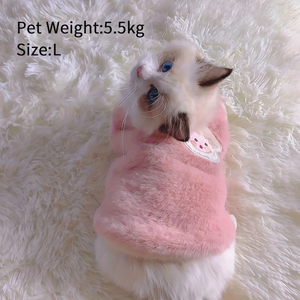 A fluffy white and gray kitten wearing a pink embroidered vest on a white, furry surface.