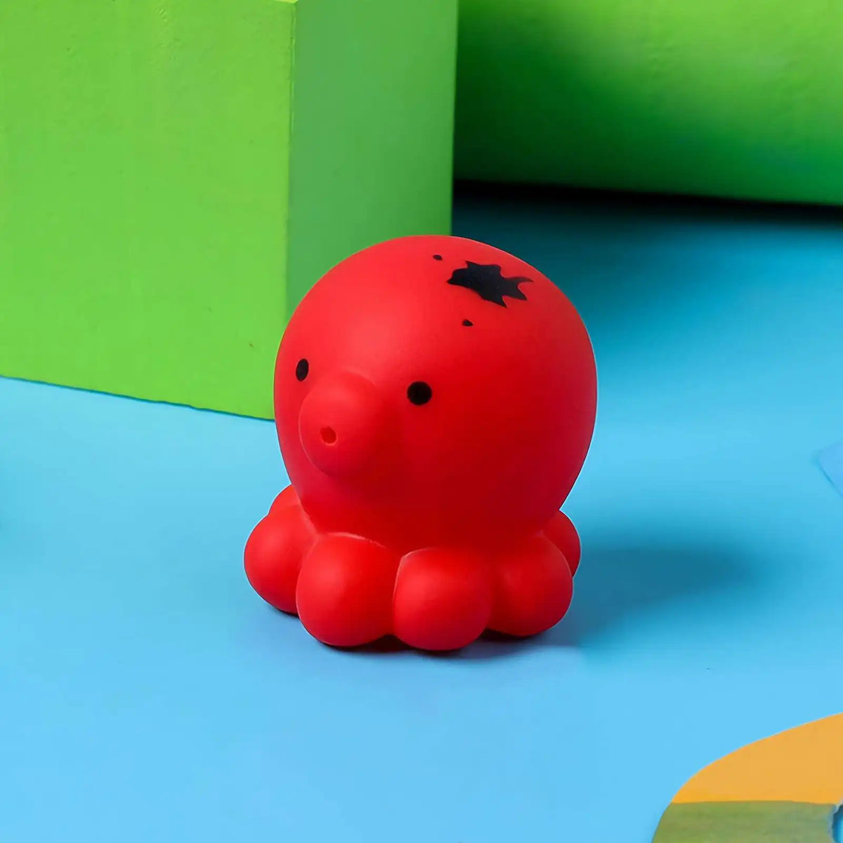 A bright red, rubbery sea life shaped product rests on a blue surface next to a green block.