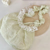 A light green floral lace bowknot shoulder bag with pleated fabric resting on a woven straw mat.