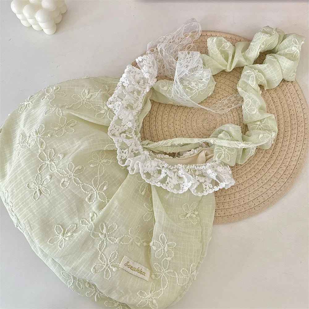 A light green floral lace bowknot shoulder bag with pleated fabric resting on a woven straw mat.